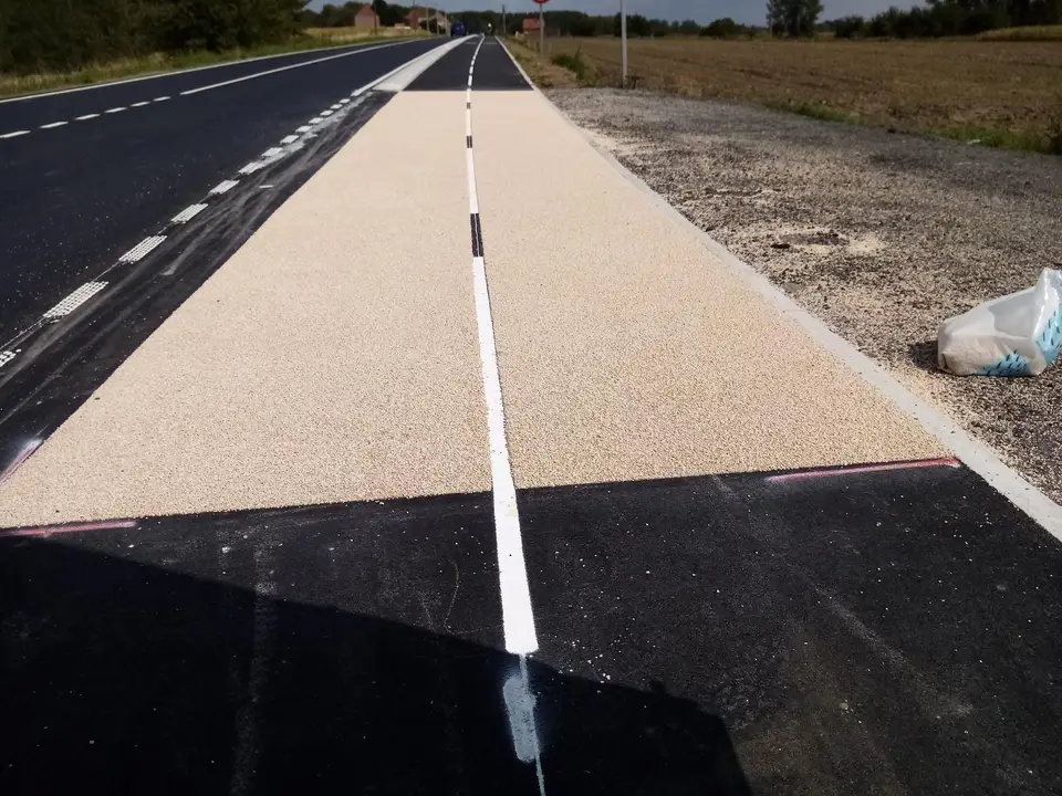 Bande beige à ligne blanche axiale le long d'une route, en bordure de champs