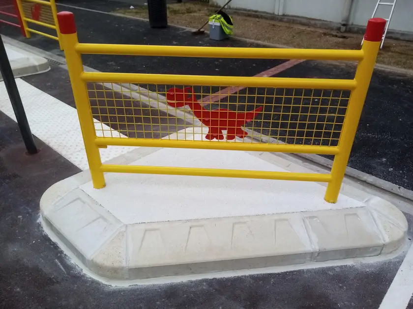 Barrière jaune à motif rouge fixée sur un socle béton, à côté d'une bande d'éveil de vigilance