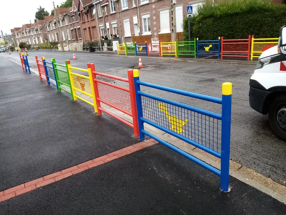 Barrières multicolores le long d'un trottoir, dans une rue bordée de maisons