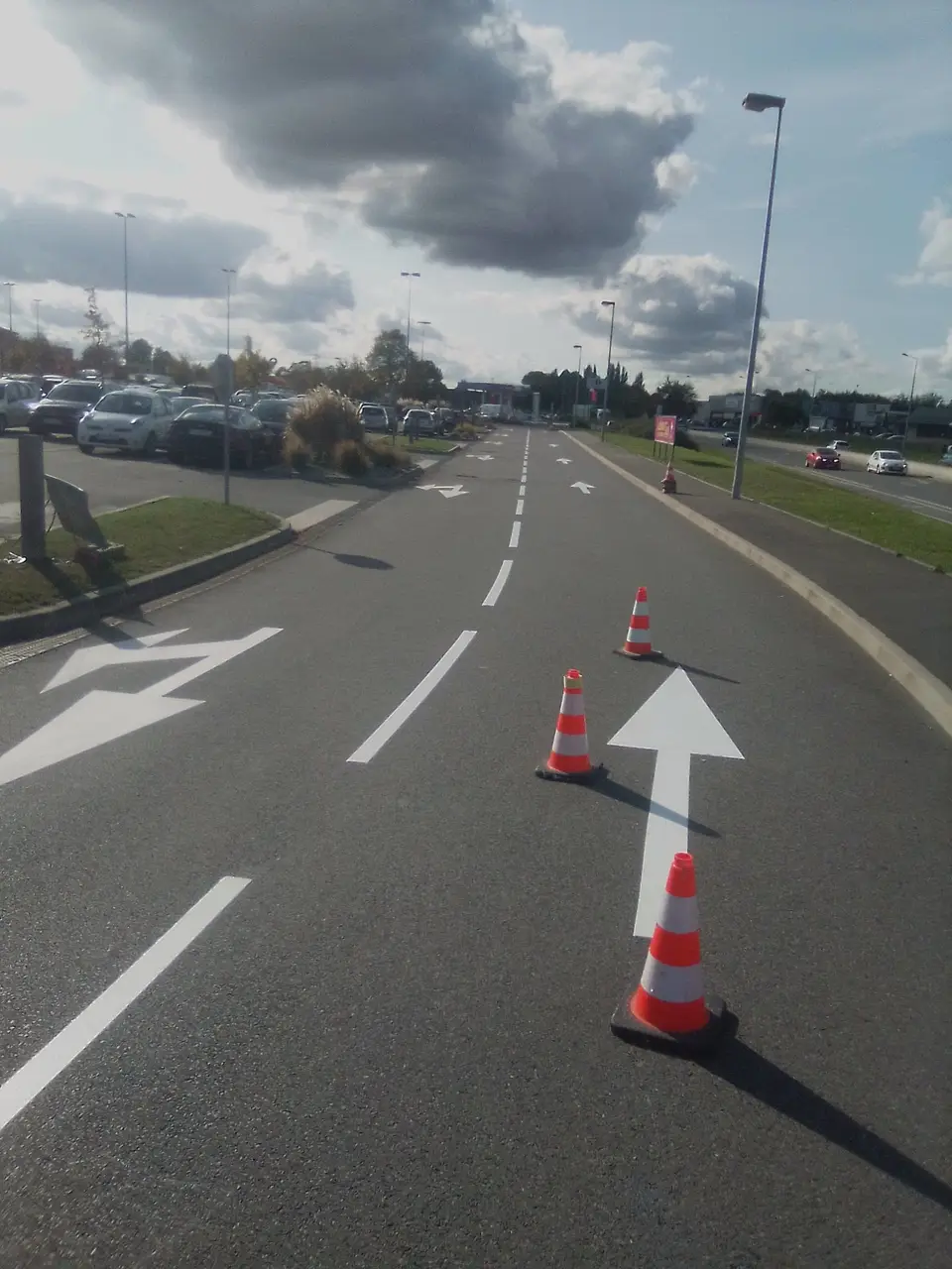 Voie à flèches directionnelles blanches, balisée par des cônes, le long d'un parking